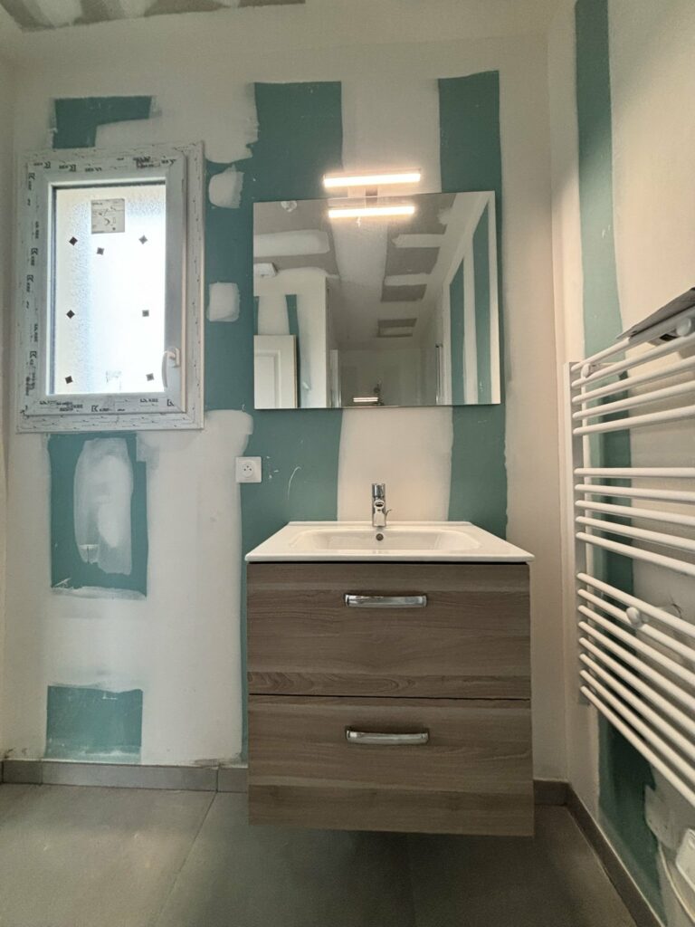 Meuble vasque et sèche-serviettes posés dans une salle de bain de maison neuve